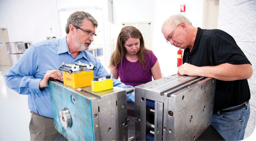 The MMD team discusses the next steps after inspecting molded parts from a development tool. The relatively inexpensive prototype mold showed what could work and how well. The production mold then incorporated all lessons learned with modifications for a more automated production. 