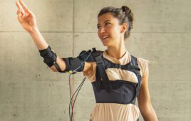 Myoshirt creator Marie Georgarakis wearing her device, which has cufs on her arm supported by a cable connected to equipment on her shoulder.