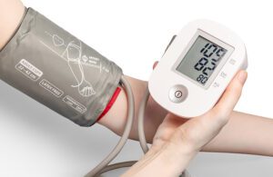 A patient holding a blood pressure monitor cuff on their arm