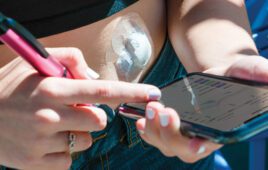 A patient wearing a continuous glucose monitor and reading the results on a smartphone while holding a smart insulin pen