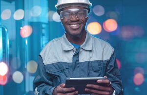 A manufacturing engineer wearing safety equipment and holding a tablet device