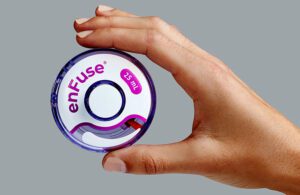 A hand holding the Enable Injections disc-shaped Enfuse device.