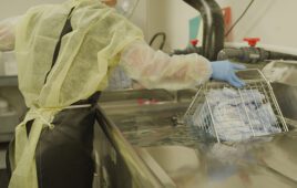 A photo showing a medical device reprocessing worker submerging a basket of used products into a bath.