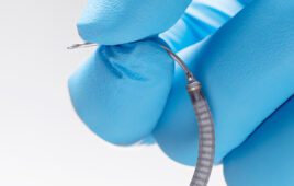 A photo of Intuitive's Flexision biopsy needle between two gloved fingers.