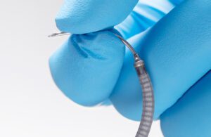 A photo of Intuitive's Flexision biopsy needle between two gloved fingers.